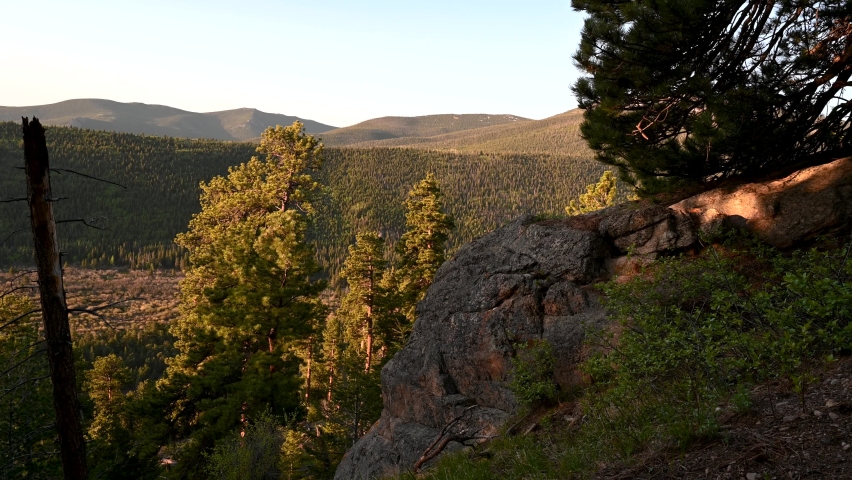 A hiker enjoys sunrise at an overlook of vast forests and mountains in the Wild Basin of Rocky Mountain National Park, Colorado, USA