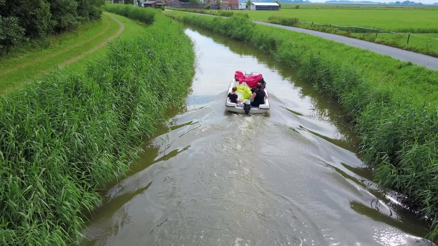 Woman and girl sailing on a small river in the countryside of the Netherlands. Driving a motorboat on a stream. Drone shot. Aerial view of a vessel in Dutch rural landscape.