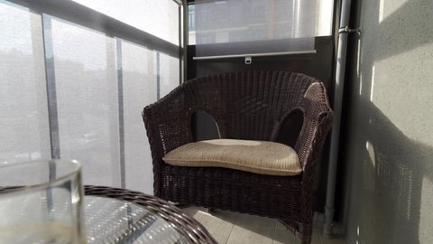 Apartment balcony with rattan furniture and gray roller blinds on the windows on a sunny day. High quality 4k footage