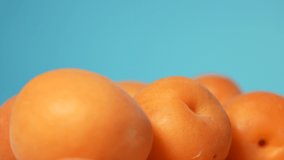 Close-up side view 4K stock video footage of many bright fresh whole juicy orange organic apricots isolated on light blue background. Fruits spinning around slowly