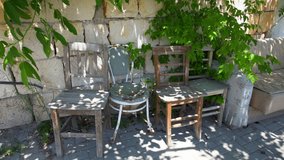 Closeup view 4k stock video footage of several old used broken chairs and sofa standing outdoor on sidewalk near stone wall of fence or building