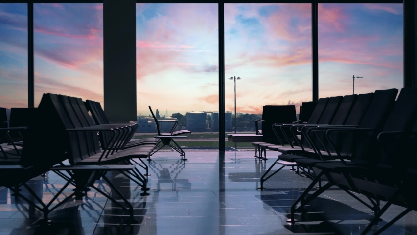 Airplane taking off seen through airport window. Sunset view from inside an empty terminal, gate waiting hall seats or benches with no people in the lounge and nobody at the gate.  Royalty-Free Stock Footage #1074071738
