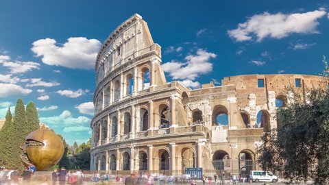 Many tourists visiting The Colosseum or Coliseum timelapse hyperlapse, also known as the Flavian Amphitheatre in Rome, Italy. Green lawn and monument. Blue sky with clouds at sunny day