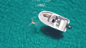 Aerial - Young couple enjoying their day on a boat on a beautiful turquoise sea. Man relaxes in the water by floating on the surface - Powered by Shutterstock - Get 15% off with code: PIKWIZARD15