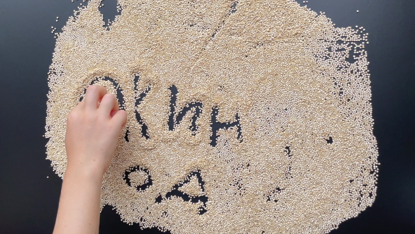 A little boy is writing letters on a blackboard covered with quinoa seeds