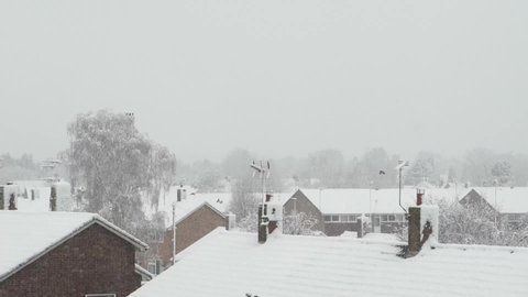 Snowy roofs of residential UK houses and distant treeline grey Winter sky