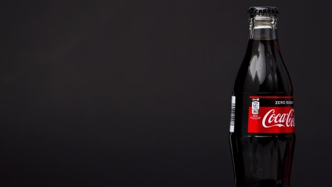 Estonia, Tallinn - March 2021: glass bottle coca-cola zero sugar drink rotating on isolated dark black background. Sparkling coca-cola soda rotating 360 degree, closeup wit copy space