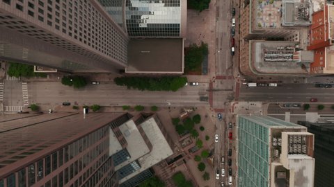 Aerial birds eye overhead top down view of wide multilane downtown street leading between tall commercial buildings. Horizontally panning view. Dallas, Texas, US