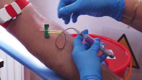 Skilled Professional Nurse in Blue Latex Gloves Collecting Blood Sample from Caucasian Male Patient using Single Use Venipuncture Needle and Switching Multiple Vacuum Test Tubes Containters
