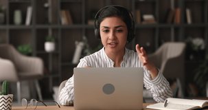Confident Indian woman sit at desk looks at laptop talk to client distantly by videoconference call. Provide help, professional counsel aid remotely. Virtual meet, solve business use videocall concept