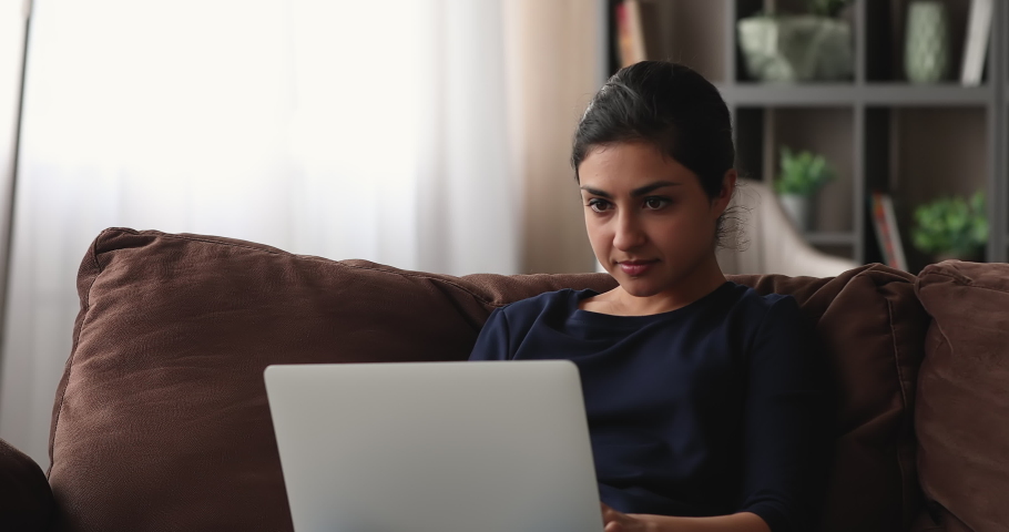 Indian woman sit on sofa work on laptop feels desperate having unexpected device malfunction. Female read awful online e-mail news. Unsaved important information, need pc repair, system error concept Royalty-Free Stock Footage #1074104579