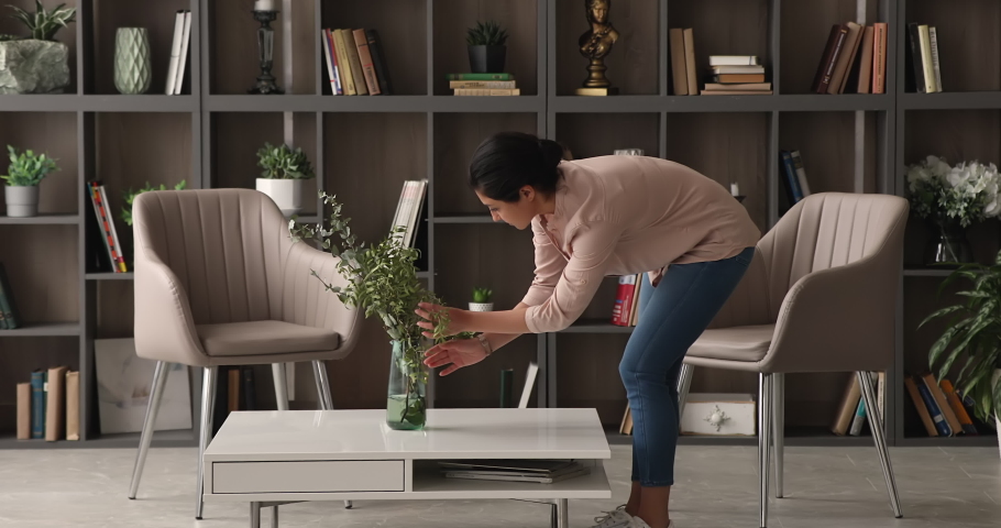 Young Indian woman bent over coffee table straighten bouquet in vase. Professional female decorator improve styling living room interior with flower arrangement. Housewife and housework chores concept | Shutterstock HD Video #1074110189