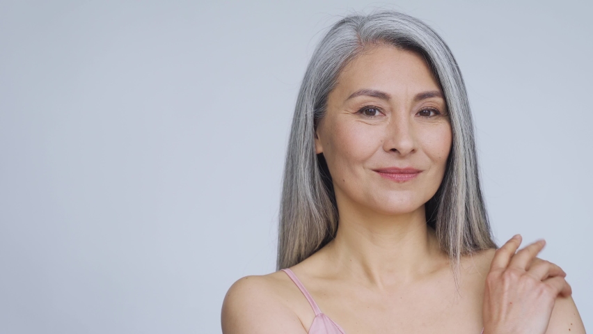 Middle aged happy mature asian woman, senior 50 year lady flirty looking away, smiling at camera, isolated on white closeup face portrait. Ads of antiaging whitening dry skincare, plastic surgery. | Shutterstock HD Video #1074124091