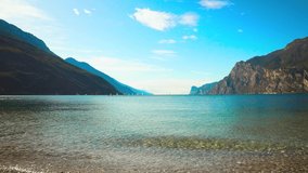 Lake Garda in Torbole Nago resort. Windsurfer Surfing Wind On Waves, Recreational Water Sports. Lago di Garda Benaco. Bright video footage, blue sky white clouds clear water waves Mountains Alps Italy