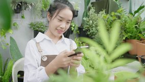 Happy asian woman taking a picture of plants and sending to her customer by smartphone, sitting in the garden at home. Girl chatting with customer. Selling online concept