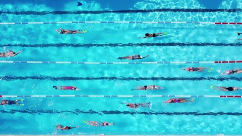 Top view group young swimmers training in swimming pool with marked lanes outdoor.Many sportive kids swim in Open Water Swimming pool with clean blue water.Children practice at summer sports camp