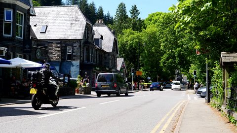 BETWS-Y-COED, WALES, UNITED KINGDOM - CIRCA JUNE, 2021: Cars, motorcycles, van carrying kayak and people passing camera point of view, POW on Holyhead Road in a popular Welsh tourist resort in summer.