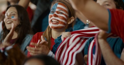 USA soccer supporters cheering in stands. Woman with USA flag painted on her face sitting in crowd cheering for her team.
