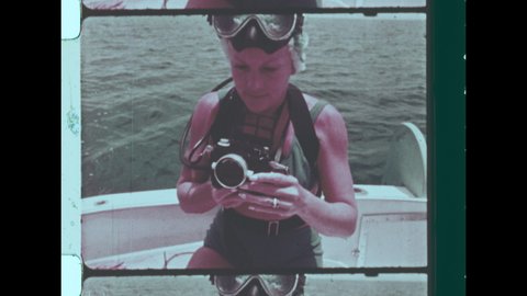 1960s Costa Brava, Spain. Woman on boat prepares Medium Format Camera for Underwater Photography. Woman wears Fashionable Green Bikini.  4K Overscan of Vintage Archival 16mm Film Print