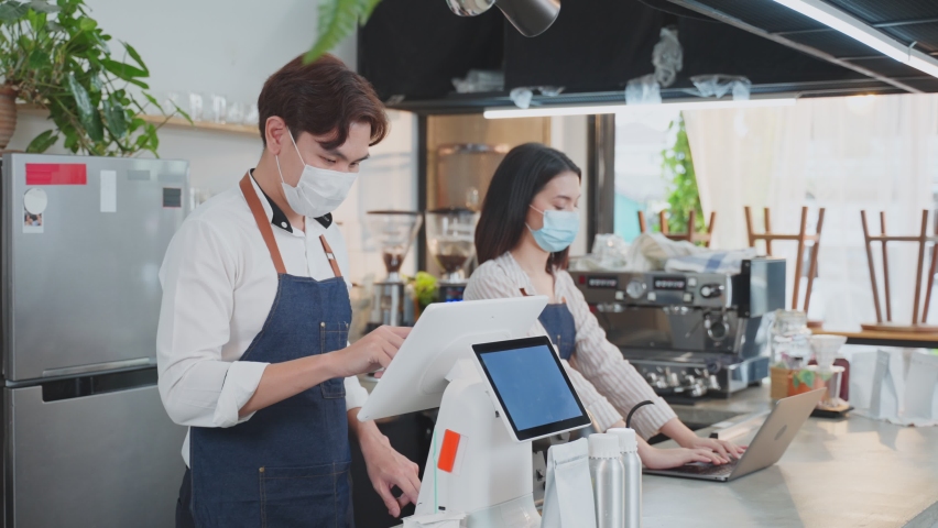 Asian cafe owner couple wear face mask due to Covid19 pandemic, check in sale order from laptop computer on counter bar in restaurant feel happy for income. Entrepreneur and Economic of small business Royalty-Free Stock Footage #1074135407