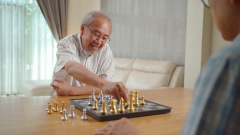 Asian Senior Elderly male spend leisure time, stay home after retirement. Happy smiling Old man enjoy activity in house playing chess game with friend together. Hospital Healthcare and medical concept