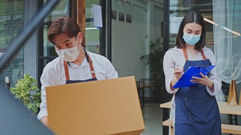 Asian cafe business owner couple wear mask due to Covid-19 pandemic, work in coffee shop. Waiter loads Parcels into car with waitress girl check on clipboard. Delivery Purchased transportation concept