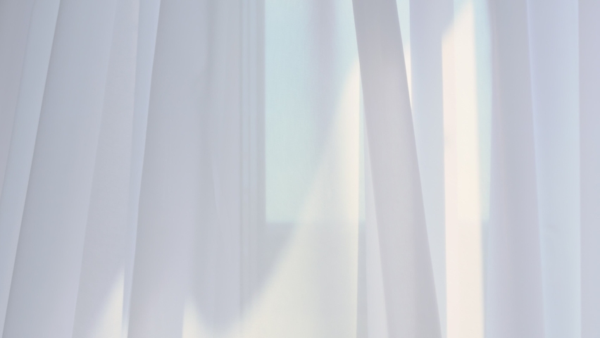 The window is covered with a white tulle curtain. Tulle curtains add home coziness and comfort. Kind sunlight seeps through the tulle curtain. The tulle necklace sways gently. Royalty-Free Stock Footage #1074137942