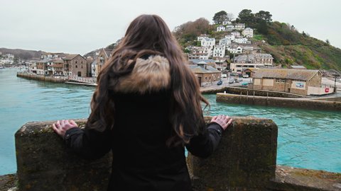 A tourist girl enjoying watching a beautiful location with houses by blue river.  A harbour with boats in old British town Looe with a dream vacation look in Cornwall, England in 4K.