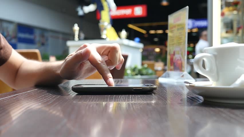 Typing sliding smart phone at cafe table during waiting for order