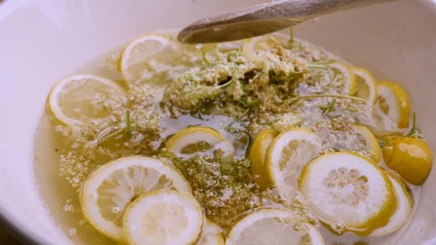 Elderflower and lemon wedges combine with sugar and water to make a delicious elderberry syrup. A spoon stirs all the ingredients.

