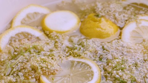 Elderflower and lemon wedges combine with sugar and water to make a delicious elderberry syrup. The camera makes a pan over the  ingredients.
