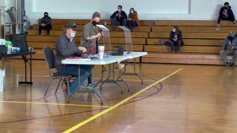 Kanab , Utah , United States - 12 07 2020: Man wearing face mask sits at a desk in a school gymnasium spinning a raffle drum and pulls a lottery number to hike the Wave (Kanab Utah)
