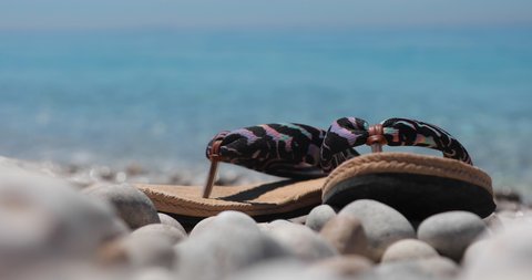 Vacation concept shot, flip-flops on tranquil pebbles beach with emerald sea background