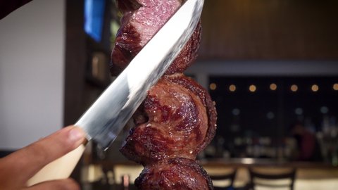 Man slices picanha traditional beef fillet steak at Brazilian steakhouse, HD