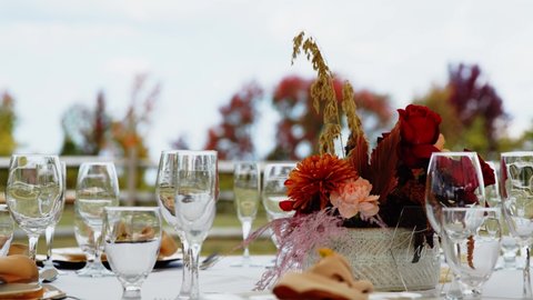 Wedding centerpiece flowers sway in breeze by fancy glasses on outdoor table