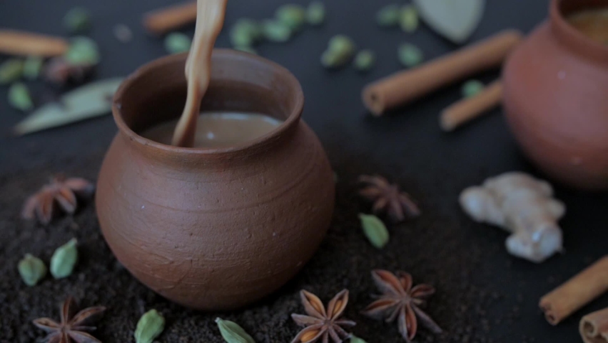 Tasty homemade boiling hot tea poured in traditional clay cups - Indian culture. Famous spices Elaichi, Tej Patta, Dalchini, and cloves kept together against a blurred background - tea-making ingre... Royalty-Free Stock Footage #1074167651