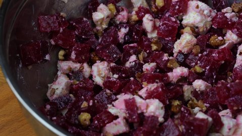 Chef is stirring a salad of boiled beetroot, feta cheese, walnuts and olive oil in a metal bowl, close up
