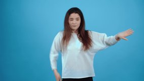 The young brunette, charismatic freestyle, wave with her hands, hip-hop freestyle, displays a wide smile. Asian with dark hair, dressed in a blue blouse, isolated on a dark blue background in the