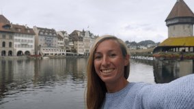 Young woman travelling in Switzerland lakes a video selfie with Luzern bridge and old town in the background. Female travelling in Luzern, Switzerland taking selfies 