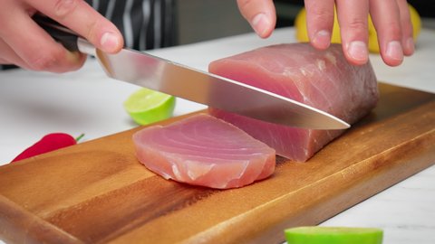Slicing raw tuna yellowfin on a table into a big steak size in 4K. Healthy meat, fresh tuna being cut in pieces on a chopping board for a tuna steak.