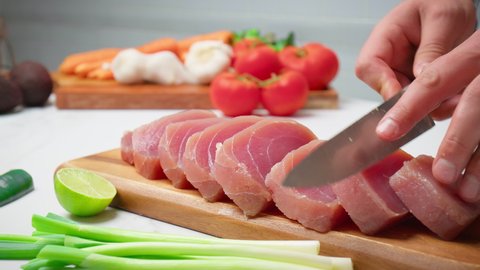 Slicing raw tuna yellowfin on a table into a big steak size in 4K. Healthy meat, fresh tuna being cut in pieces on a chopping board for a tuna steak.