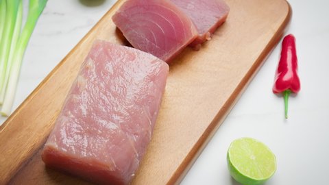 Sliced Raw Tuna Yellowfin on a cutting board with greens and vegetables in 4K. Healthy meat, fresh tuna cut in pieces on a chopping board by a chef.