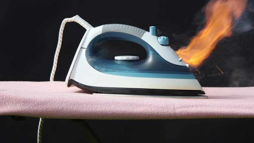 Faulty home appliance is burn, an iron for clothes has caught fire on ironing board.