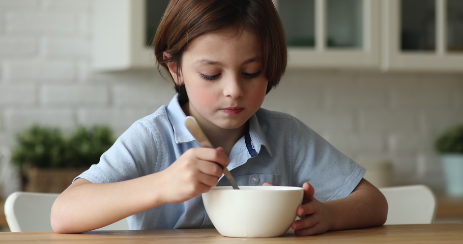 Close up sluggish little boy sit in kitchen look sick, without appetite, does not want eat corn flakes with milk. Loss of apetite, picky in meal, bad mood, not tasty breakfast, eating disorder concept Royalty-Free Stock Footage #1074180461
