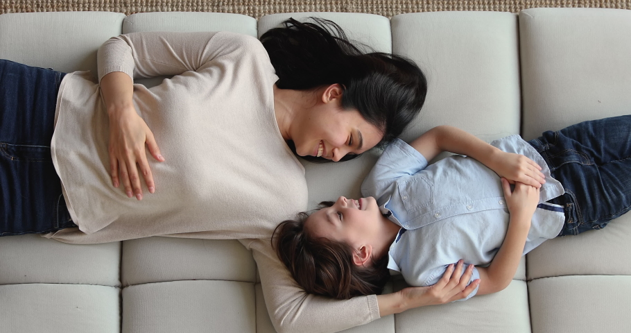 Young serene Vietnamese mother adopted little preschooler adorable son, calm multi ethnic family lying on couch, overhead view. Happy tender moments together, life value, custody and foster concept Royalty-Free Stock Footage #1074180611