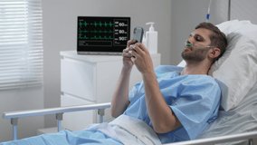 Man in hospital with the mobile phone and earphones lying alone in bed. Male Patient Using Mobile Phone In Hospital Bed