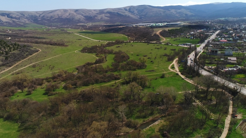 Charming small town located in the green valley, ecological place for living. Shot. Picturesque natural landscape with meadows, green trees and mountains far in the distance.