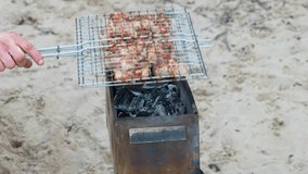 man's hand cooking meat on a barbecue grill at the sand beach. Grilling Bbq at sunny day on a portable grill 4k video