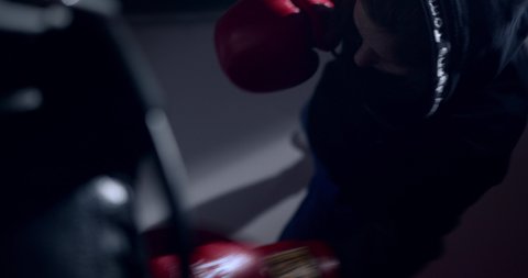 Ukraine, Kiev, April 2021 Woman boxer in boxing gloves hits a punching bag with quick punches in a dark gym. A close-up of the pear and the blows on it can be seen.