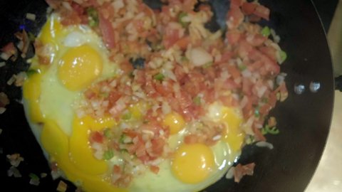 Top view of raw eggs and classic pico de gallo in frying pan. Frying eggs, chopped tomatoes, onion, and chili peppers for delicious Mexican-style scrambled eggs dish. Traditional meal preparation